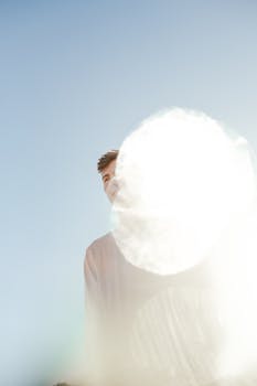 这是一幅富有创意的肖像，描绘了一位年轻人，背景是明亮的蓝天，镜头还捕捉到了耀斑