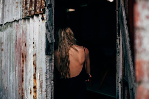 Back view of anonymous female with long hair standing in shabby door of aged building
