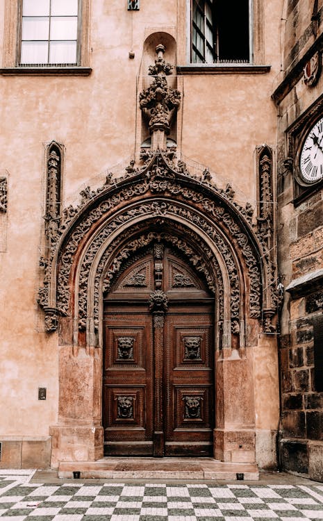 Exterior of aged building with arched carved entrance with wooden doors and clock on old street