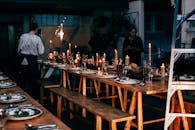 Anonymous women serving wooden tables with plates and glassware among burning candles while preparing for banquet in modern place