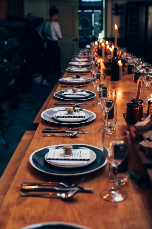 Free From above of long served wooden table with plates and cutlery near elegant glassware among burning candles in modern cafe Stock Photo