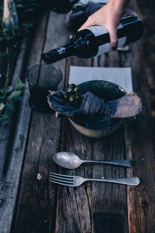 Free From above of crop anonymous person pouring wine from bottle in glass near plate decorated with blackberries on wooden table Stock Photo