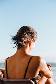 女人穿着泳装，在海滩上享受着一个阳光明媚、宁静祥和的日子，湿漉漉的头发映衬着晴朗的天空