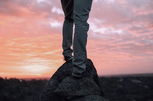 Crop anonymous person on rough rocky terrain near forest under sky with clouds in sunset