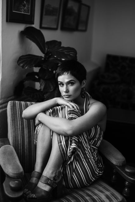 Black and white of young female with short hairstyle in striped trendy dress looking at camera in armchair in lounge