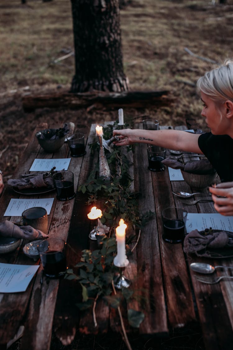 Woman Serving Table With Candles And Wine In Garden