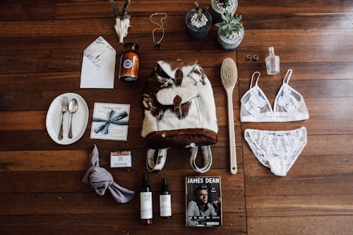 From above of cow skin backpack arranged with feminine skin care items and lingerie and postcard on timber floor in daytime