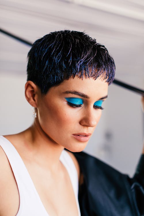 Young content female with stylish haircut and bright makeup with blue eyeshadows looking down