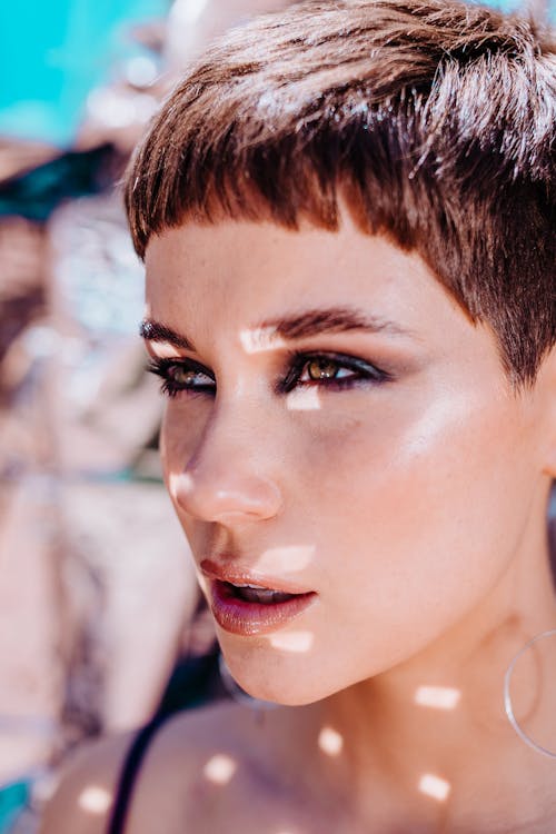 Crop alluring young female with makeup and dark short hair standing on street on sunny day and looking away