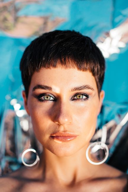 Graceful young lady with perfect skin and dark short hair looking at camera against bright blue background