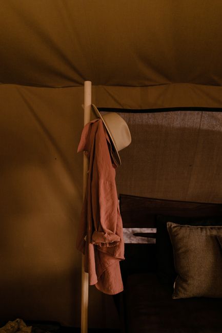 Shirt and hat hanging on wooden stand hanger in cozy tent at campsite