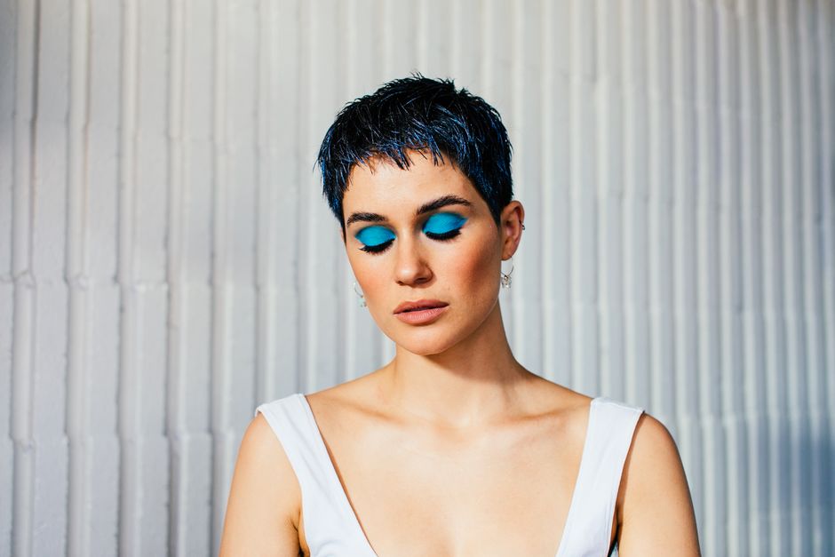 Pensive young female model with short dark hair demonstrating bright makeup with closed eyes against white wall