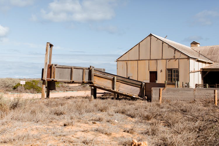 Weathered Rural Barn With Broken Fence On Semi Desert Terrain