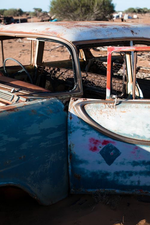 Free Fragment of old damaged automobile covered with rust with open door and peeling paint placed on ground in sunny junkyard Stock Photo
