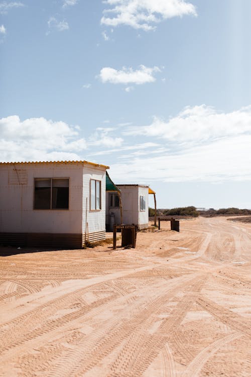 Small houses for poor located near dusty road in sunny suburb area under blue sky with clouds