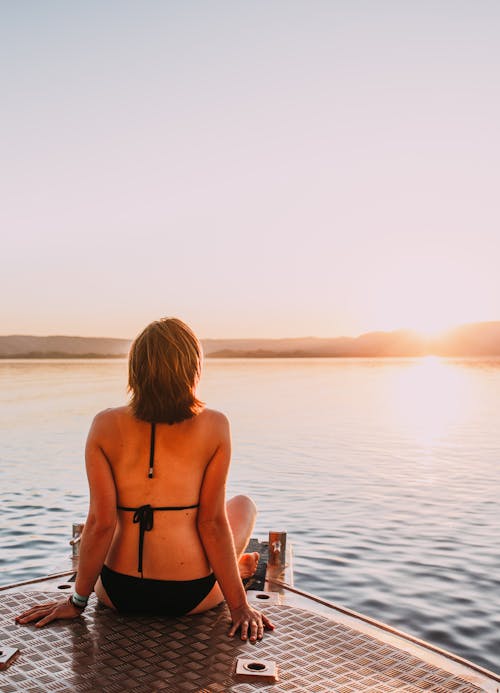 Free Woman in swimwear admiring bright sun over lake Stock Photo
