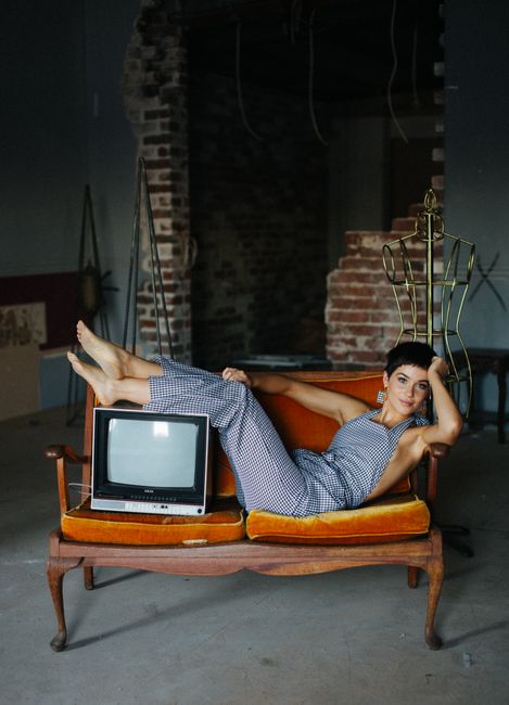 Stylish woman posing on vintage sofa with an old TV in a rustic setting.
