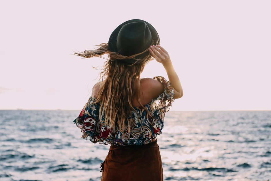 Back view of anonymous female tourist with flying hair in hat admiring waving sea during trip