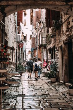 Group of tourists strolling on narrow cobblestone street of old town with shabby buildings