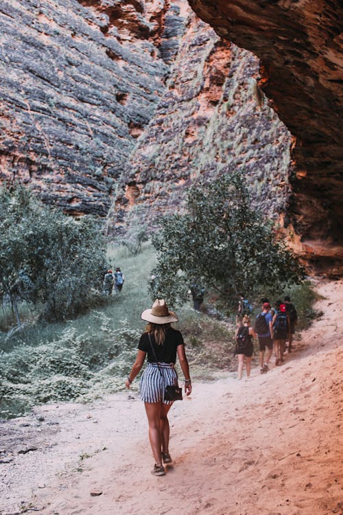 Travelers walking on sandy ground through steep stony mountains while exploring nature during trip