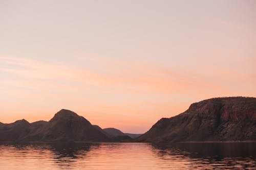 Scenery of rippling water flowing near seashore with rough mountains under colorful cloudy sky at sunset time in nature in evening