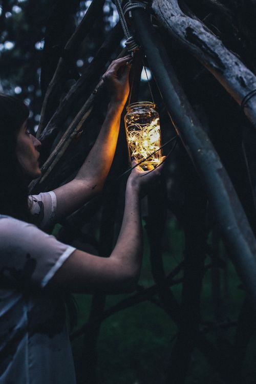 Free Side view of peaceful female hanging jar with glowing garland on wooden construction in forest during evening time in nature Stock Photo
