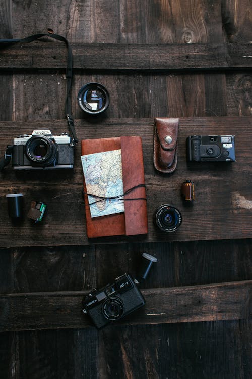 Top view collection of old fashioned photo cameras with lenses and films placed on wooden surface with notepad and map