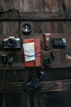 Top view collection of old fashioned photo cameras with lenses and films placed on wooden surface with notepad and map