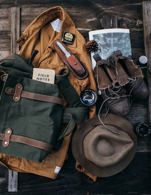 Top view of costume with hat and old fashioned boots placed on wooden surface with backpack and lens near newspaper