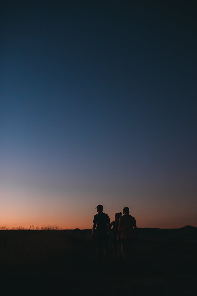 Unrecognizable Hikers Exploring Countryside Under Sunset Sky