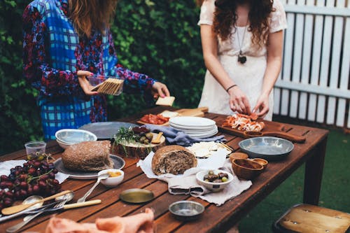 Unrecognizable women serving table with assorted appetizers in garden