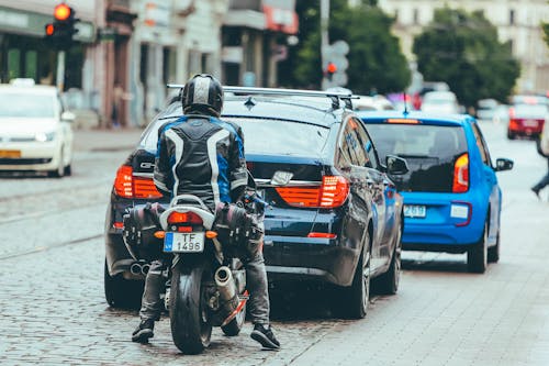 Biker riding motorcycle behind modern cars on crossroad