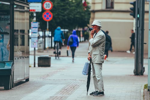 Free Full body side view of aged male with umbrella standing on pavement and thinking on question Stock Photo