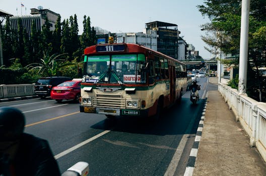 Busy Bangkok street scene featuring a classic public bus and motorbike bustling through traffic.