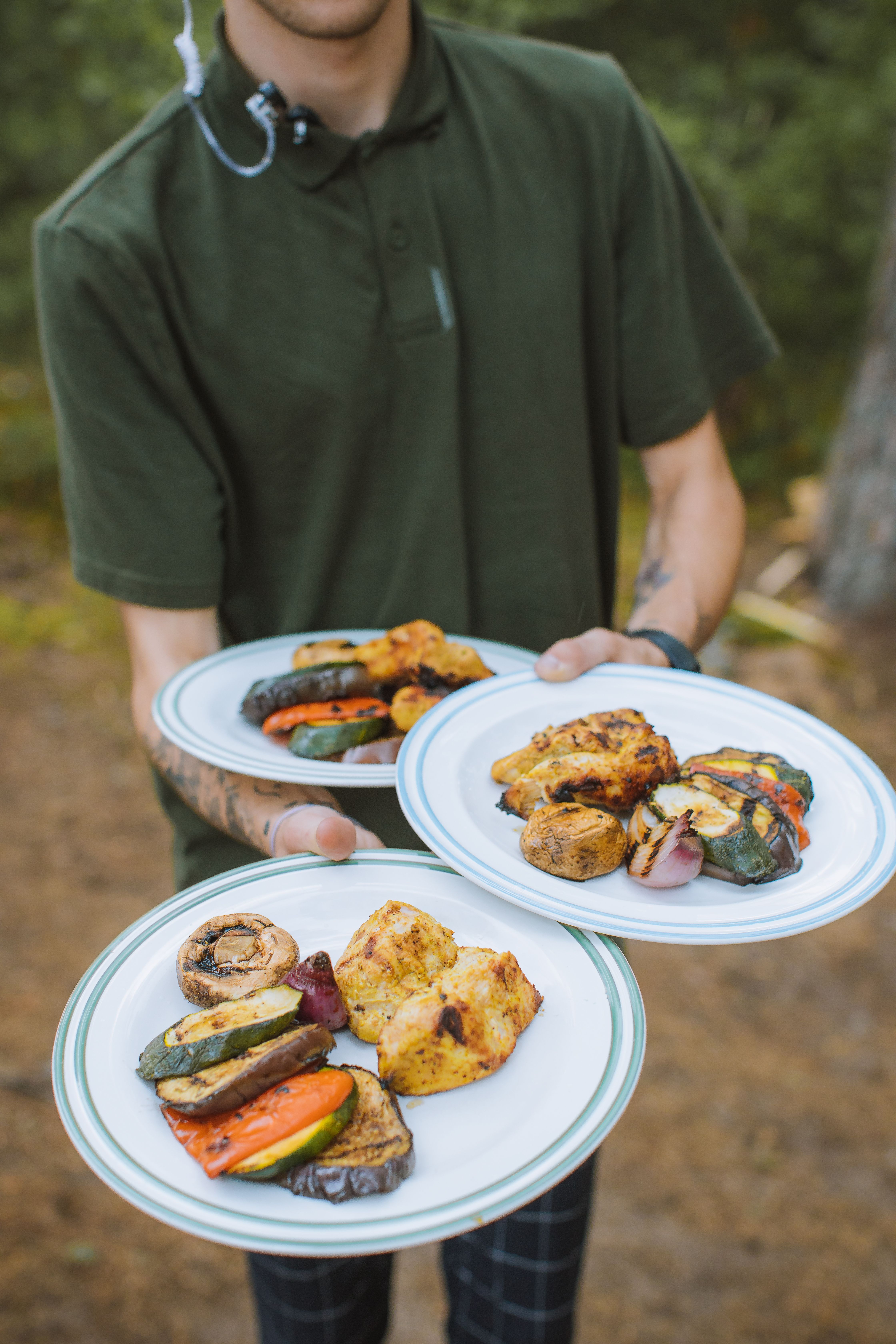 Grilled chicken breasts with visible char marks arranged on a platter next to charred zucchini, red bell pepper, and red onion, garnished with lemon wedges and fresh herbs.