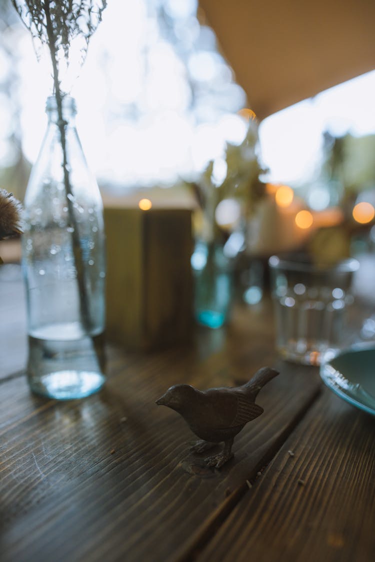 Sculpture Of A Black Bird On Wooden Table Beside Clear Glasses