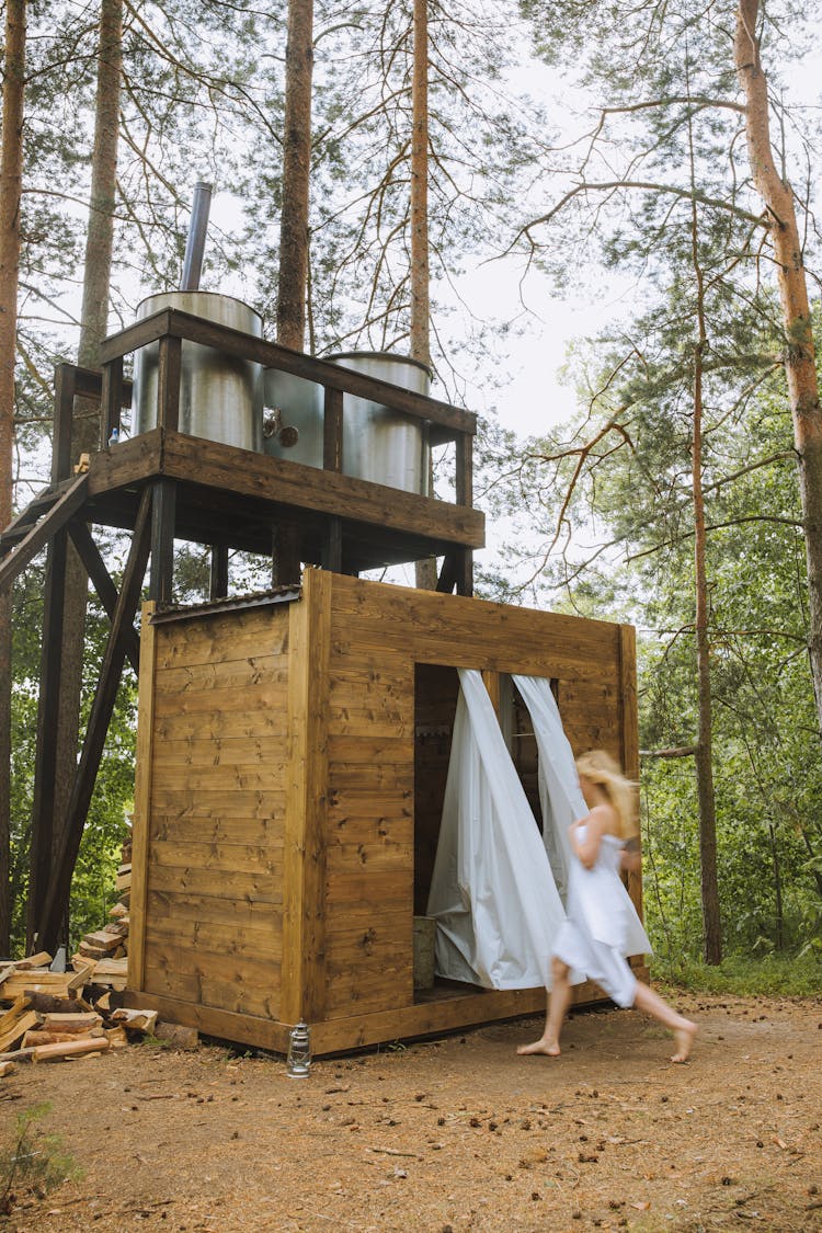 Woman In Bath Towel Running Towards An Outdoor Wooden Bathroom