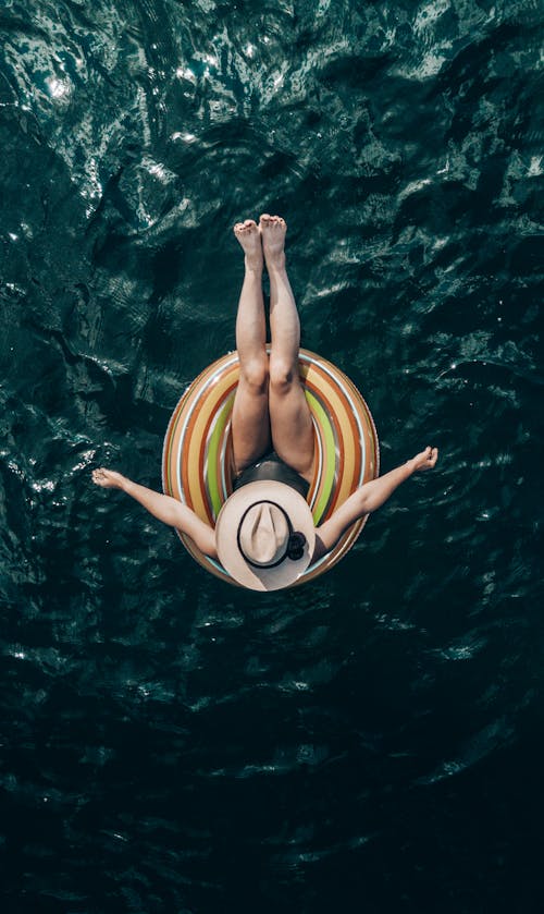 Безликая путешественница отдыхает в надувном кольце на берегу океана