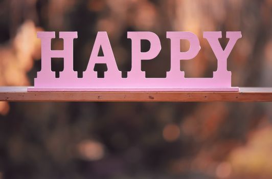Close-up of a pink 'HAPPY' sign against a warm, blurred background, symbolizing joy.