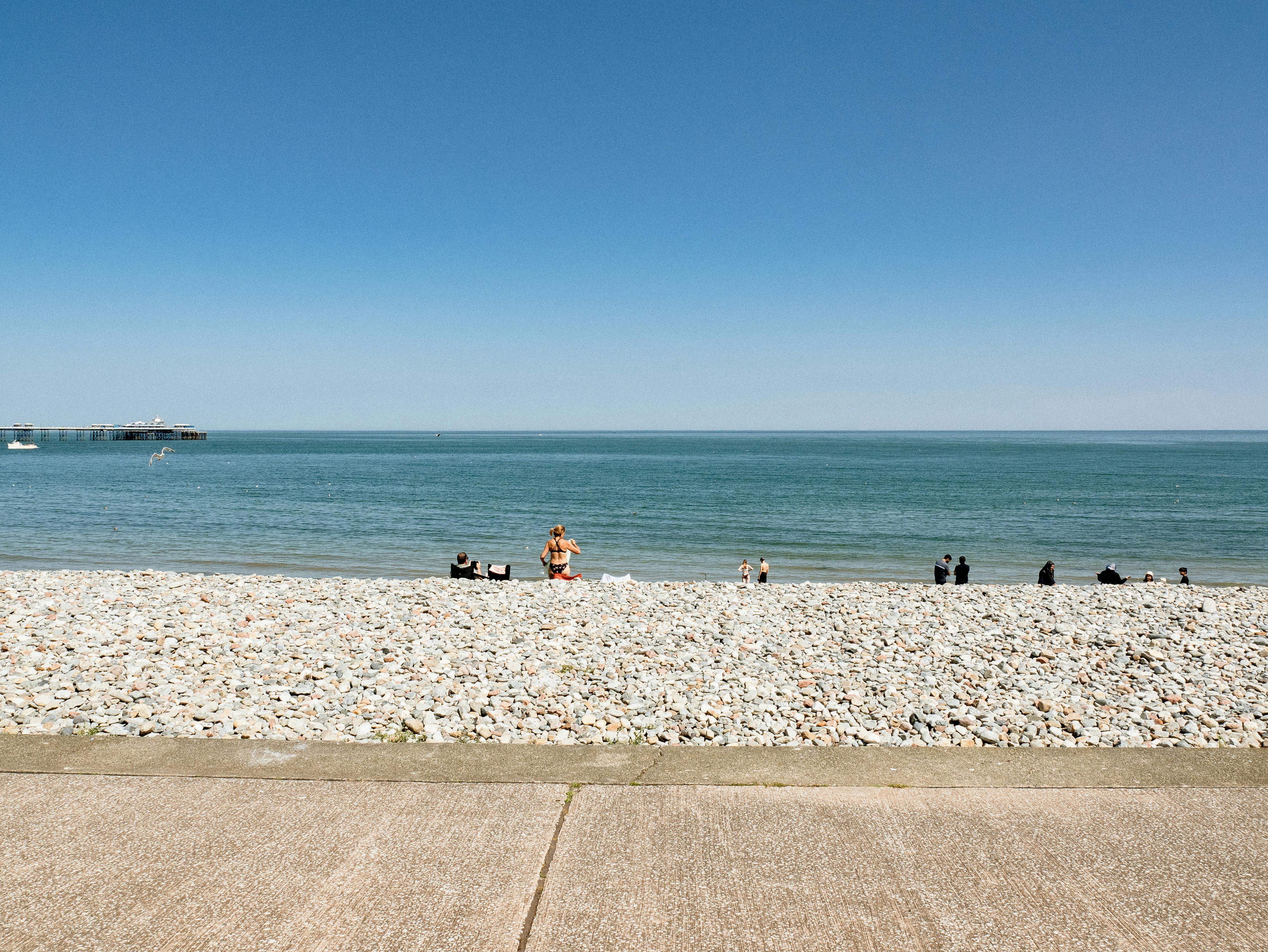 People enjoying a sunny day at the rocky Llandudno Beach in Wales, United Kingdom.
