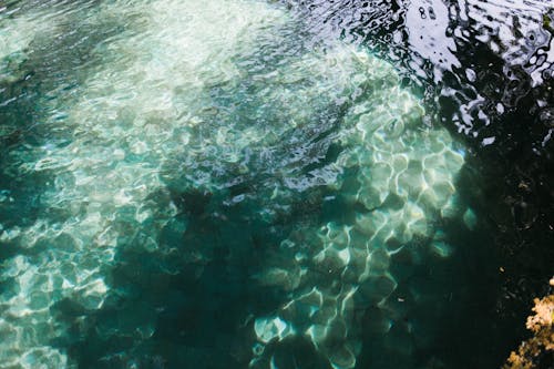 From above of vibrant glistening turquoise lake covered with ripples in shadow in daytime