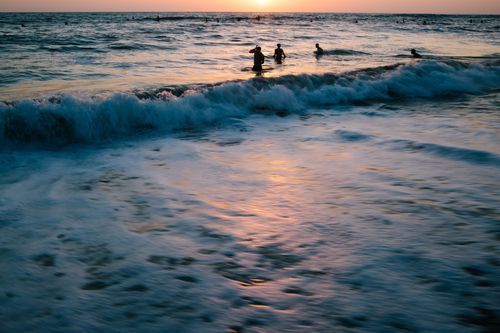 Free Long exposure of shining sun in vibrant pink sky over people swimming in blue wavy ocean in evening Stock Photo