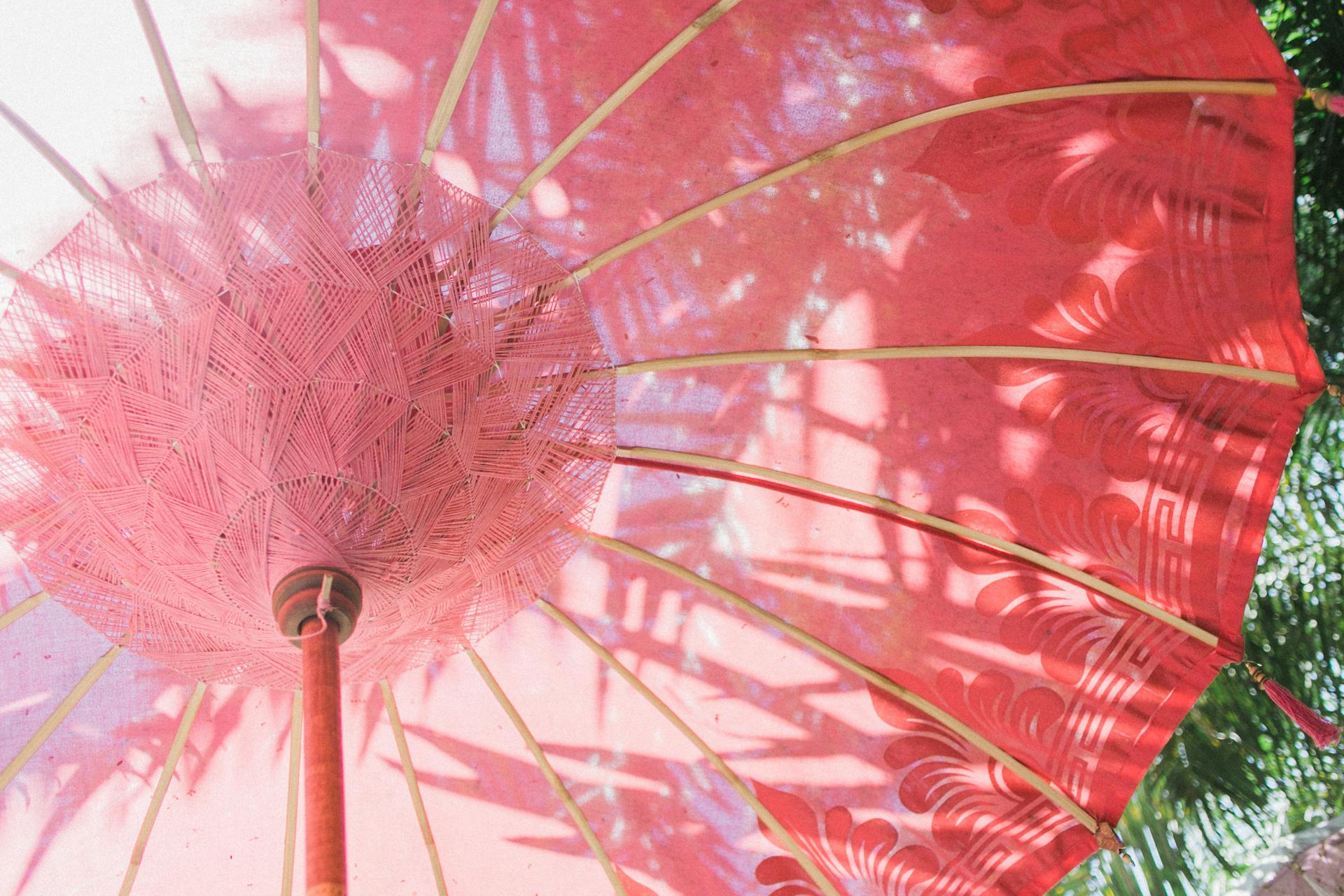 Low angle of big red umbrella with long thin wooden ribs under vibrant green leaves in summertime