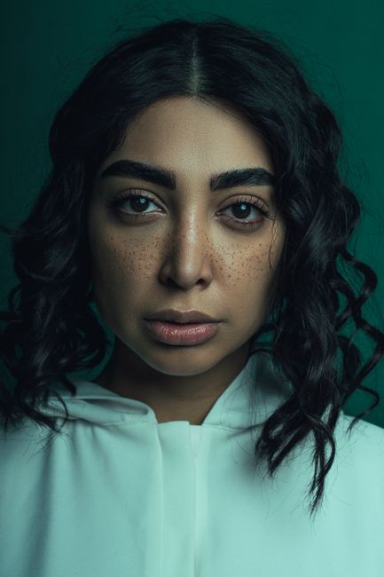 Close-up portrait of a woman with curly hair and freckles, exuding a serious expression.
