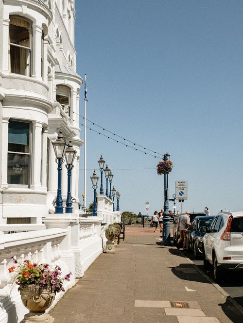 Free City street with old building and decorated pathway with potted plants near road with parked cars in sunny day Stock Photo