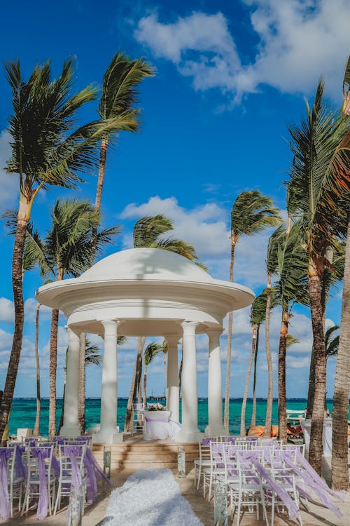 Old arbor near stools with decorative ribbons near sea under cloudy blue sky during festive event