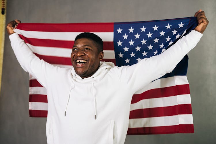 Close-Up Photo Of A Man In A White Hoodie Holding A United States Of America Flag