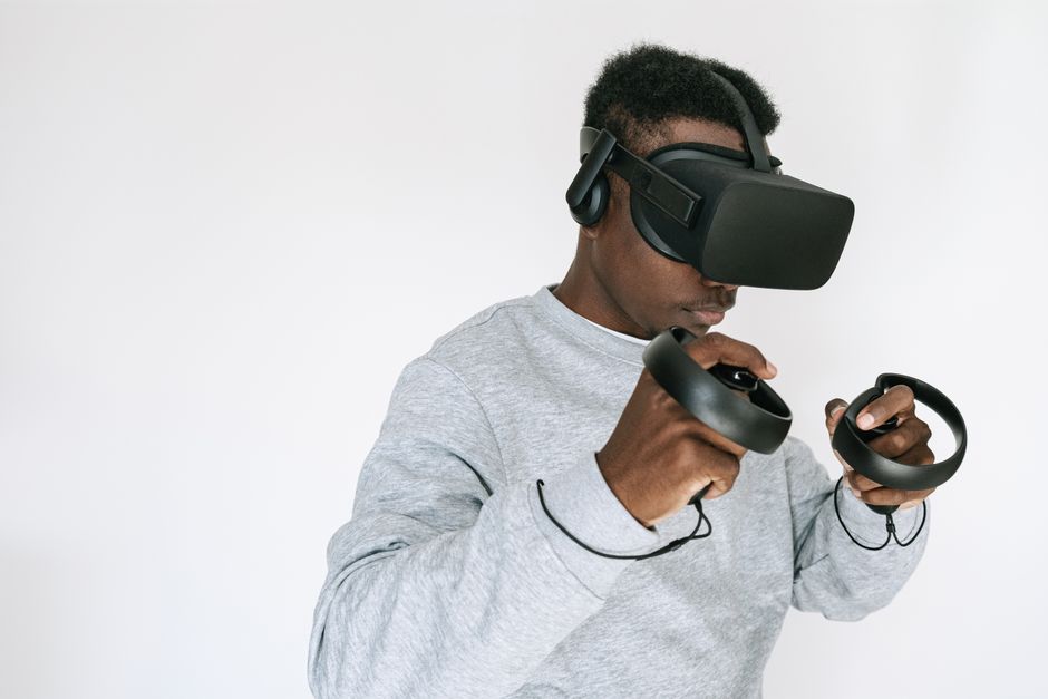 Black man wearing VR headset and controllers on a white background, exploring virtual reality.