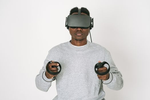Man in gray sweater interacts with virtual reality using VR headset and controllers.