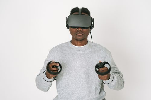 Free Man in gray sweater interacts with virtual reality using VR headset and controllers. Stock Photo